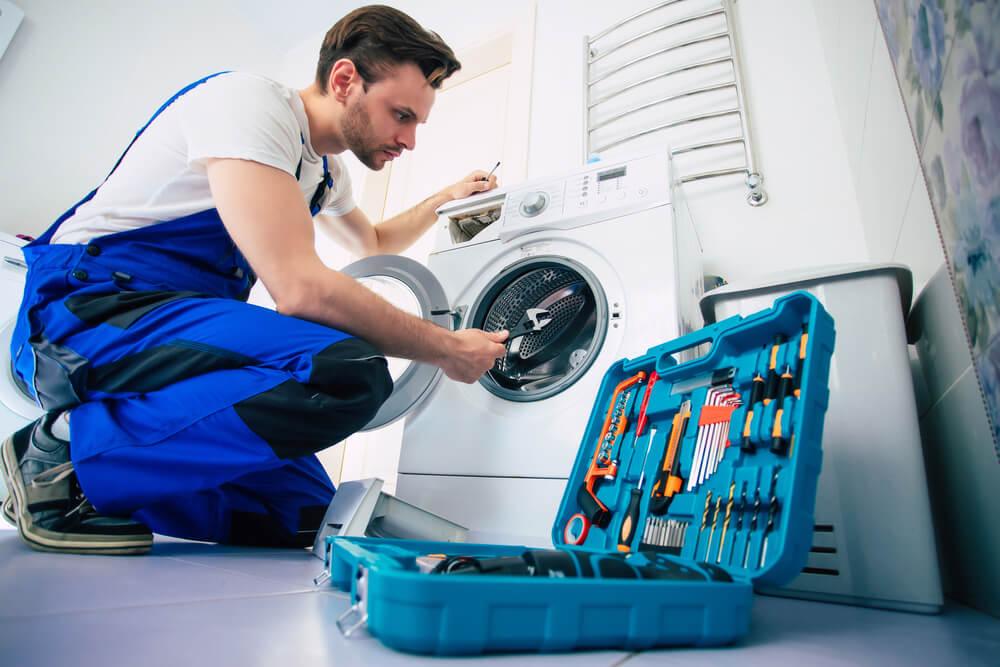 Technician repairing a washing machine in a modern laundry room, with tools spread out beside them.