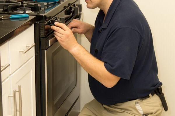 A technician repairing an oven door in a Naperville kitchen, highlighting the in-home appliance repair services from Unique Repair Services.