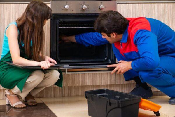 A technician and homeowner examine a broken oven in a Naperville kitchen—showcasing in-home oven repair services by Unique Repair Services.