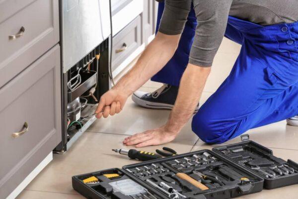 A technician kneels while repairing an under-counter oven in a Naperville kitchen—an example of Unique Repair Services' appliance expertise.